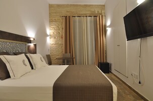 Ein Hotelzimmer mit Bett, Fernseher, kleinem Tisch und Steinwand.