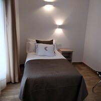 En pænt redt seng med et mørkt tæppe, et natbord og en lampe på væggen.