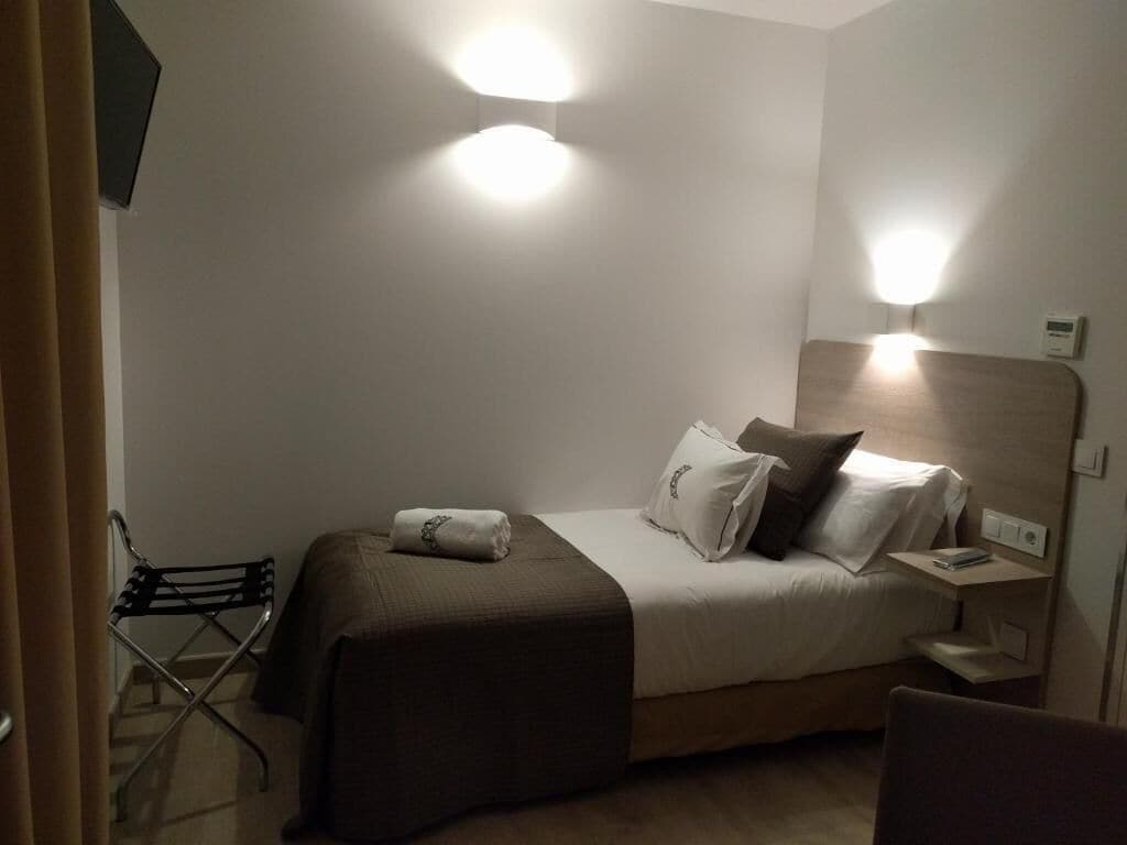 A hotel room with a bed, bedside tables, a chair, and wall-mounted lights.