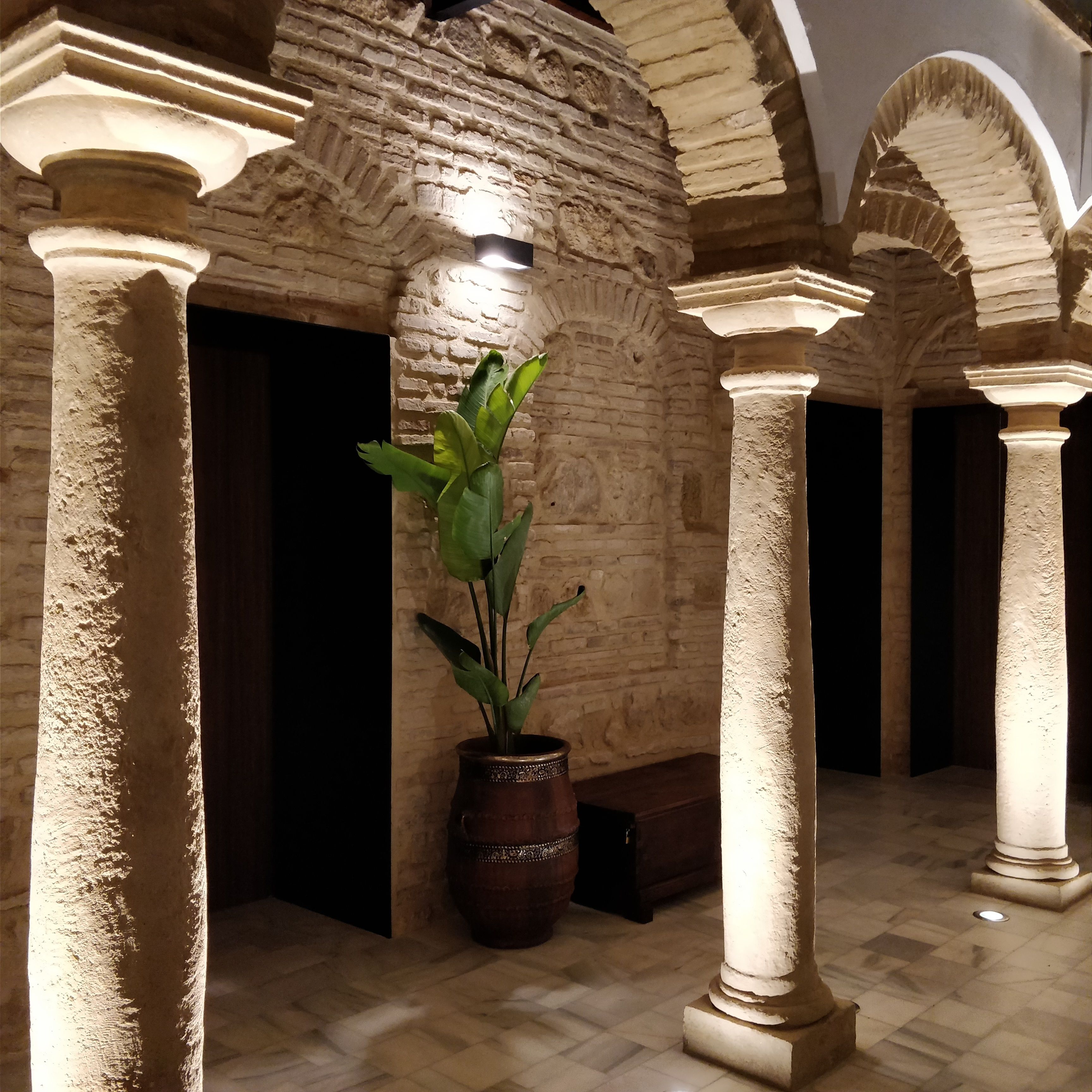 Un pasillo con columnas de piedra, una planta en maceta y una pared de ladrillo.