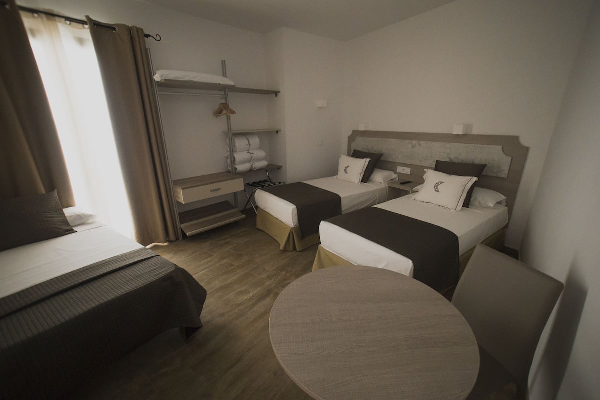 A hotel room with two single beds, a round table, a wardrobe, and a shelf with towels.