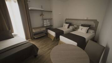 Habitación de hotel con dos camas individuales, una mesa redonda, un armario y una estantería con toallas.