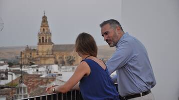 A couple standing on a balcony overlooking a historic building with a bell tower.