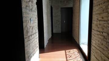 Un couloir étroit aux murs en briques apparentes et au plancher en bois, qui mène à une porte sombre.