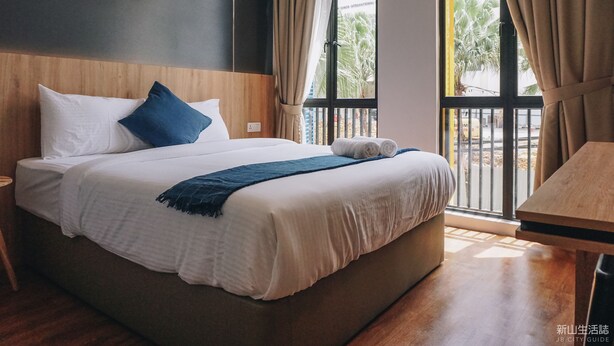 Habitación de hotel con una cama grande, cabecera de madera, ventana con cortinas y una mesa de madera.
