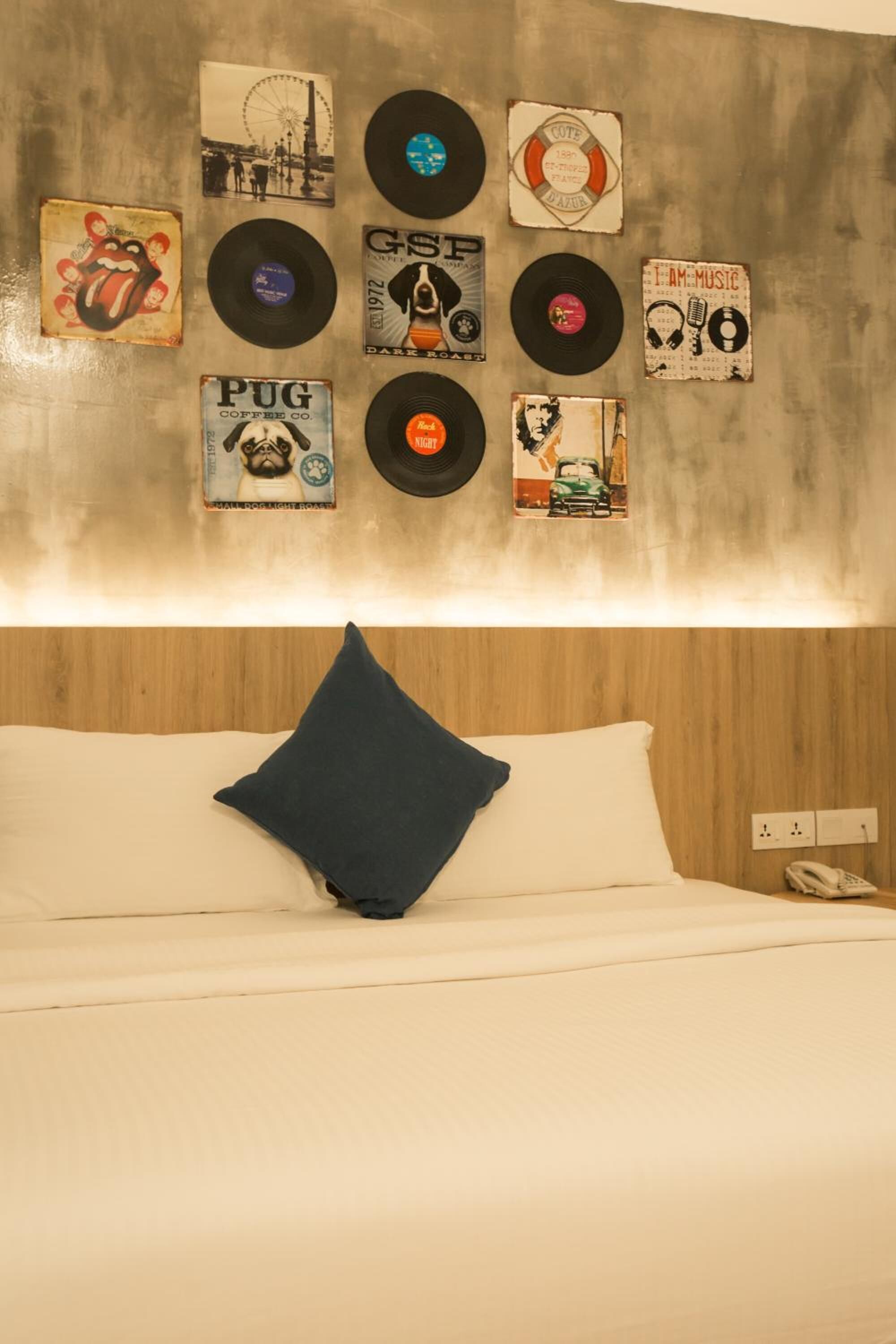 A bedroom with a bed, a pillow, and a wall decorated with various vinyl records and album covers.