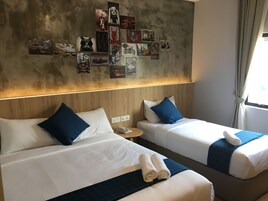 A hotel room with two beds, a wall decorated with various posters, a wooden headboard, and a window with curtains.
