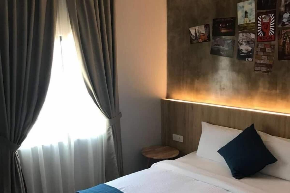A hotel room with a bed, curtains, a bedside table, and a wall with posters.