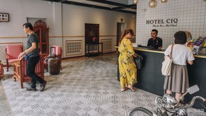 Zona de recepción de un hotel con mostrador de registro, una silla de madera, una maleta y una motocicleta.