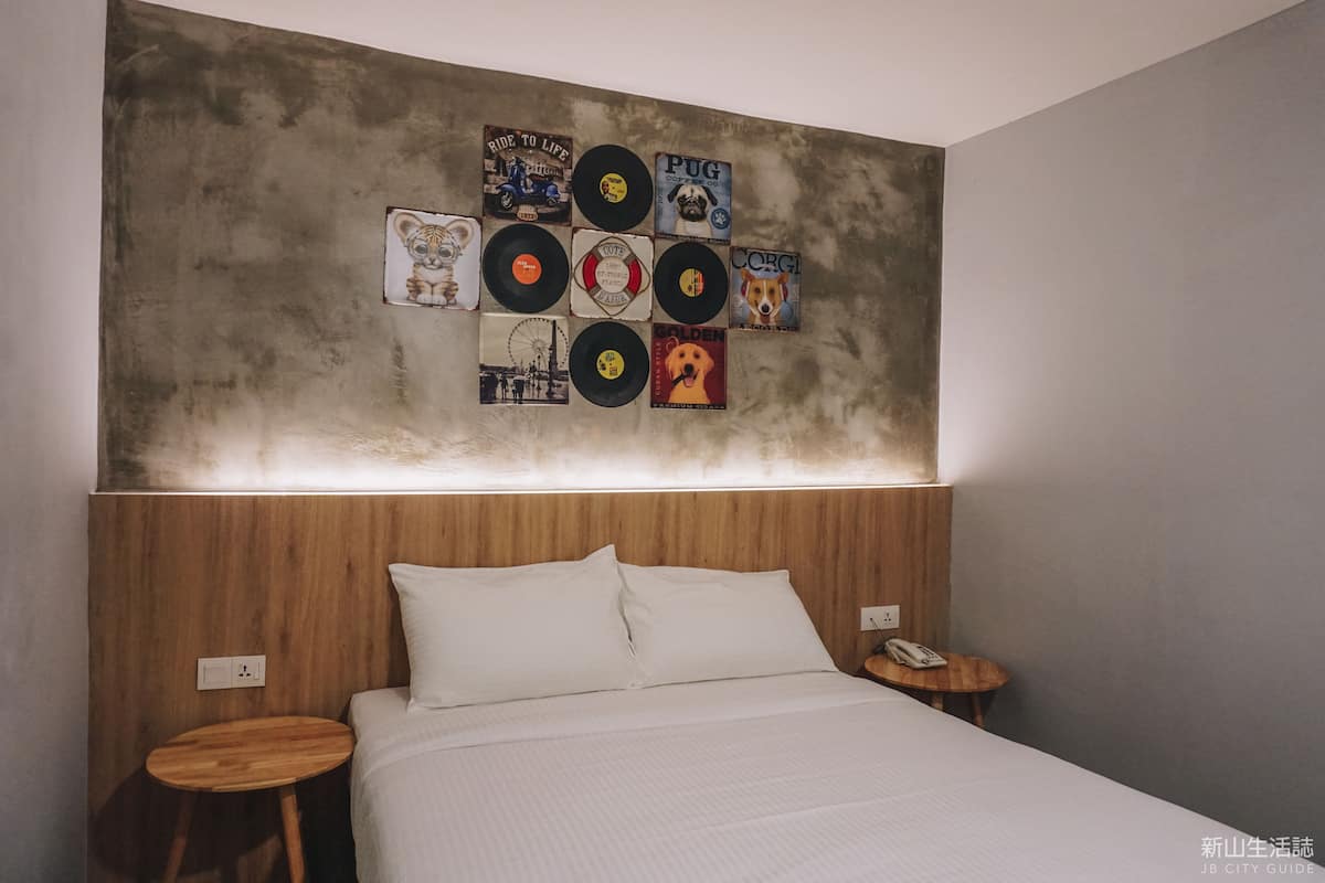 A bedroom with a wooden headboard, a bed with white bedding, a small wooden side table, and a wall decorated with vinyl records.