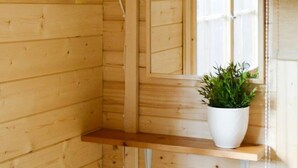 A wooden cabin interior with a window, a shelf with a potted plant, and a visible electrical outlet. - Karjamaa Camping (Parnu)