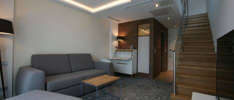A modern living room with a grey sofa, a wooden coffee table, and a patterned carpet.