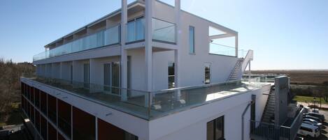 Un immeuble moderne à plusieurs étages, doté d’un balcon en verre et d’un escalier menant à l’étage supérieur.