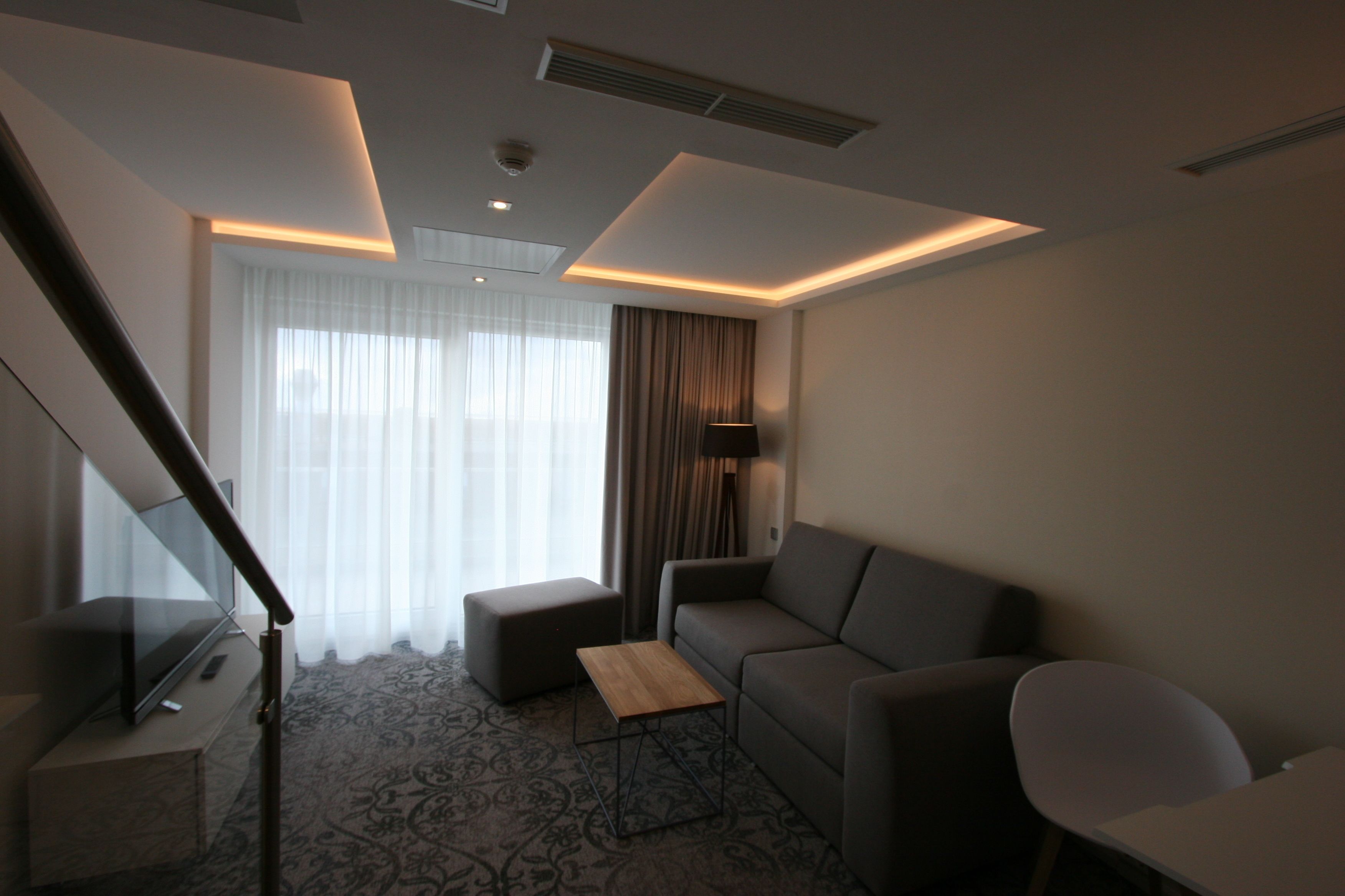 A modern hotel room with a sofa, a small table, a TV, and a staircase.