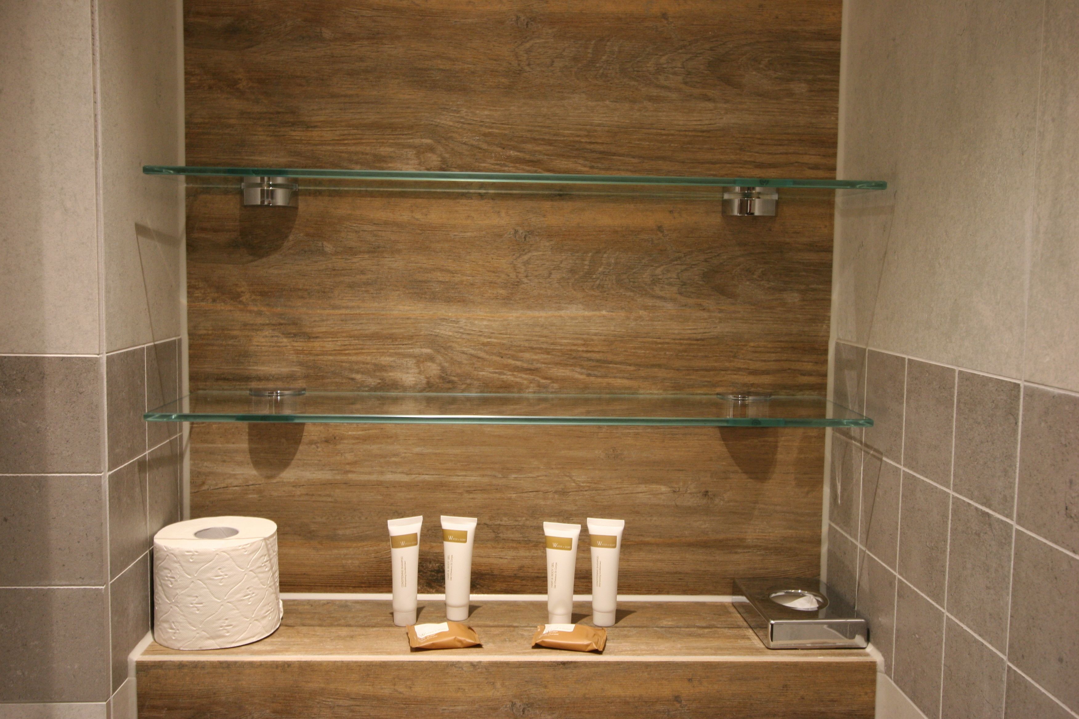 A bathroom with a wooden vanity, a glass shelf, and toiletries.