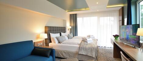 Une chambre d’hôtel avec un lit, un canapé bleu, un bureau avec une télévision et une fenêtre avec des rideaux.