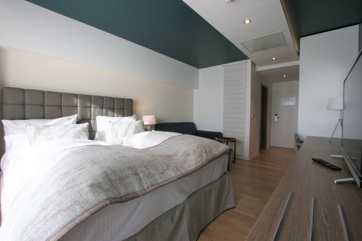 A modern hotel room with a large bed, bedside tables, a desk, and a television.