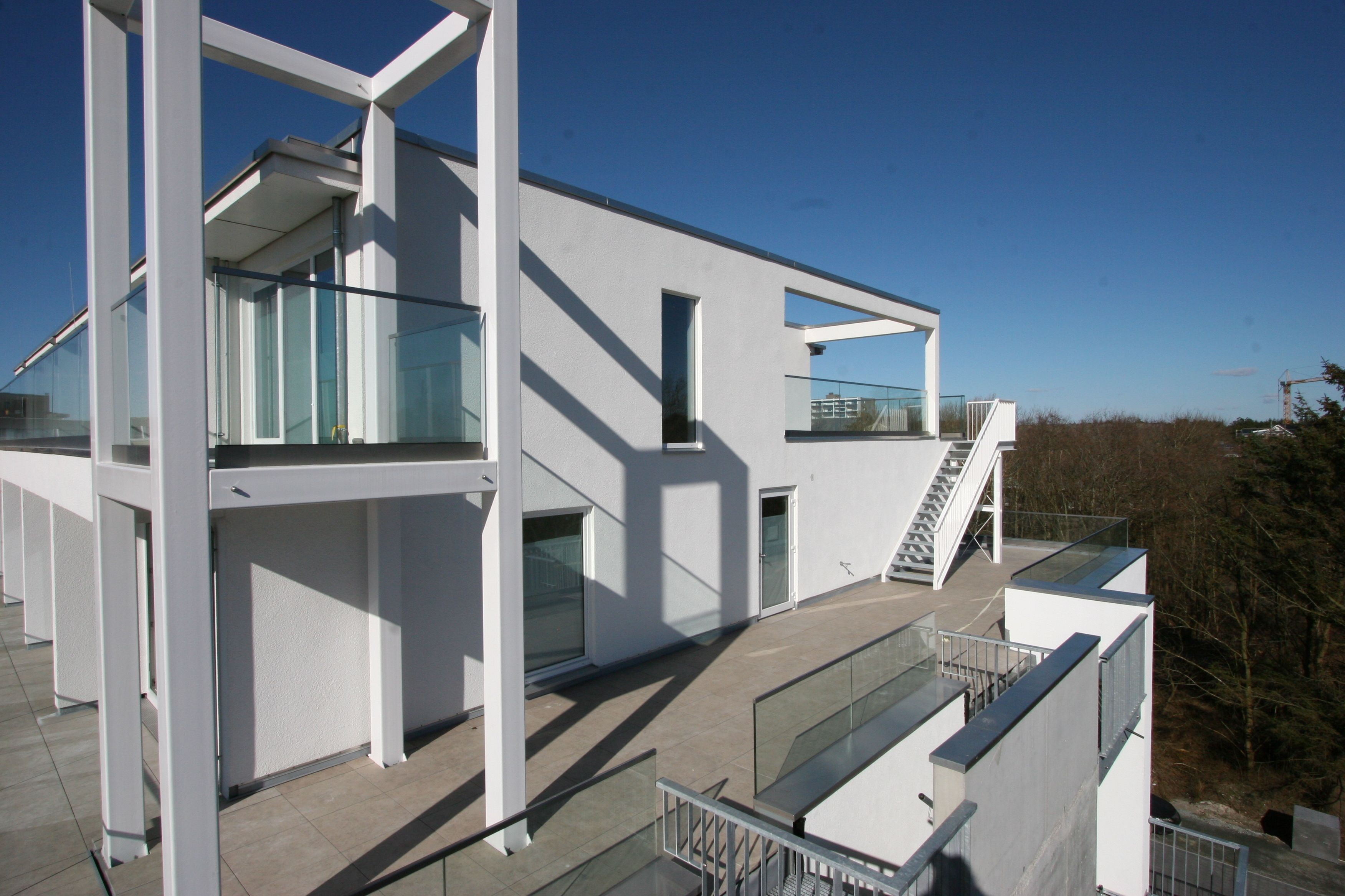A modern building with a glass facade, a staircase leading to an upper level, and a clear sky.