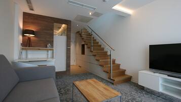 A modern living room with a grey sofa, a wooden coffee table, a flat-screen TV, and a staircase with wooden steps.