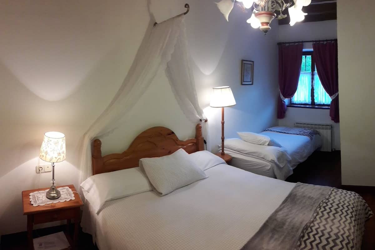 Een slaapkamer met twee bedden, een nachtkastje met een lamp, een raam met gordijnen en een radiator.