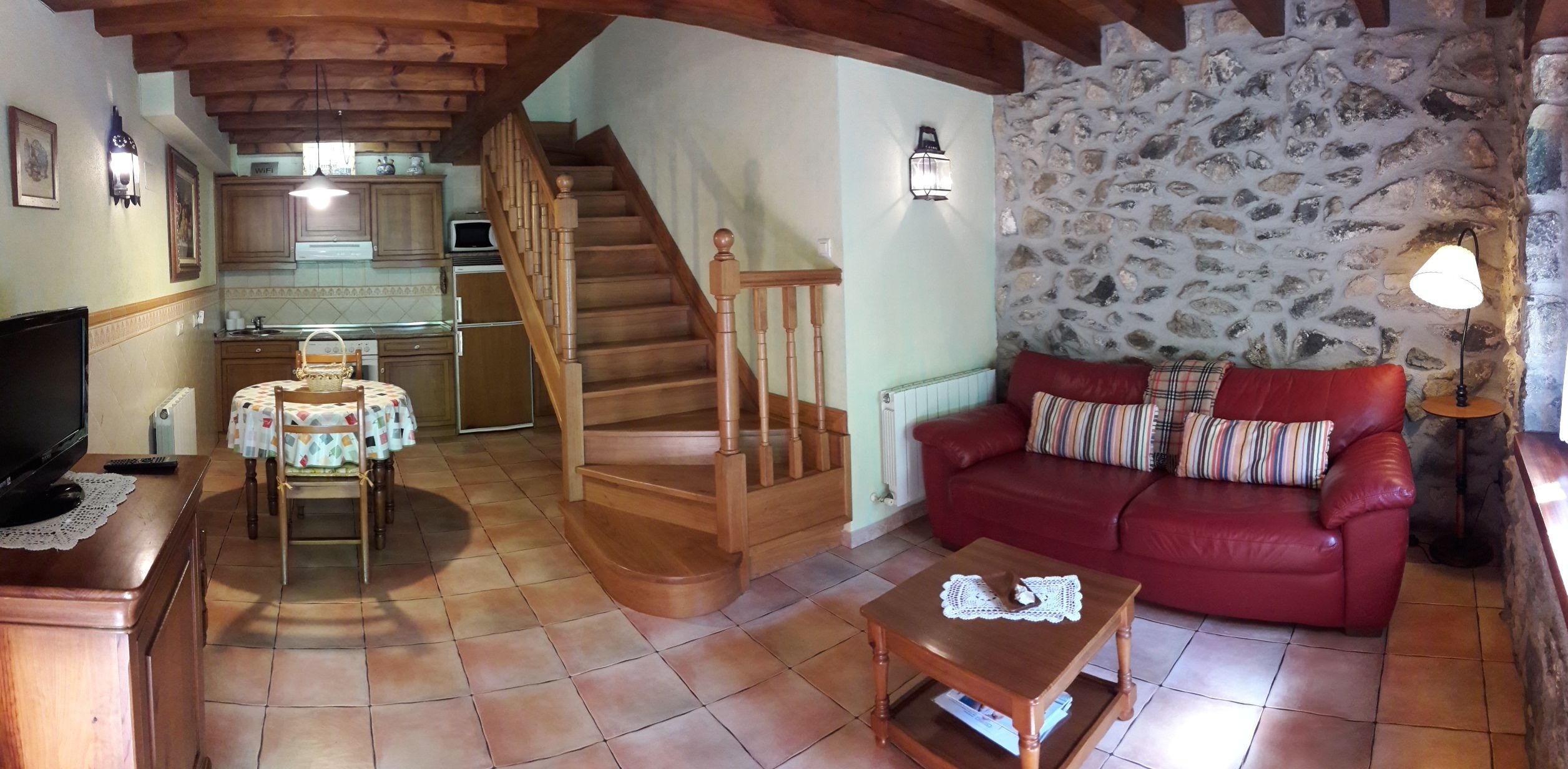 A cozy living room with a red sofa, wooden coffee table, and a staircase leading to a kitchen.