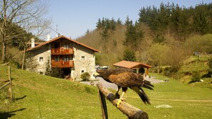 Ein Steinhäuschen mit Balkon, umgeben von einer grünen Wiese und Bäumen.
