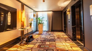 A hotel hallway with a patterned floor, a potted plant, a small table with a lamp, and an elevator. - PLAZA TERRACE  AP4065 by RIVIERA HOLIDAY HOMES (Niza)