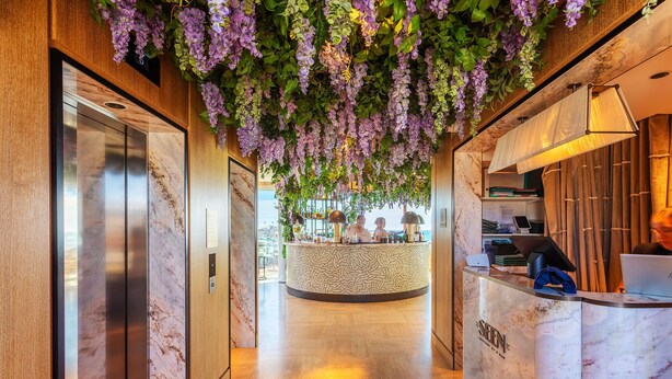 A hotel lobby with a reception desk, a marble elevator, and a hanging floral installation. - PLAZA TERRACE  AP4065 by RIVIERA HOLIDAY HOMES (Niza)