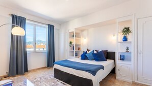 A bedroom with a bed, a desk with a lamp, a window with curtains, and built-in shelves with decorative items. - PLAZA TERRACE  AP4065 by RIVIERA HOLIDAY HOMES (Niza)