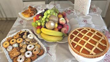 Una mesa con mantel floral, un plato de pasteles, un bol de fruta y un pastel con corteza de rejilla.