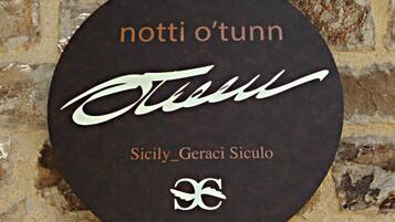 A circular sign with the text "notti o'tunn" and "Sicily_Geraci Siculo" against a stone wall background.