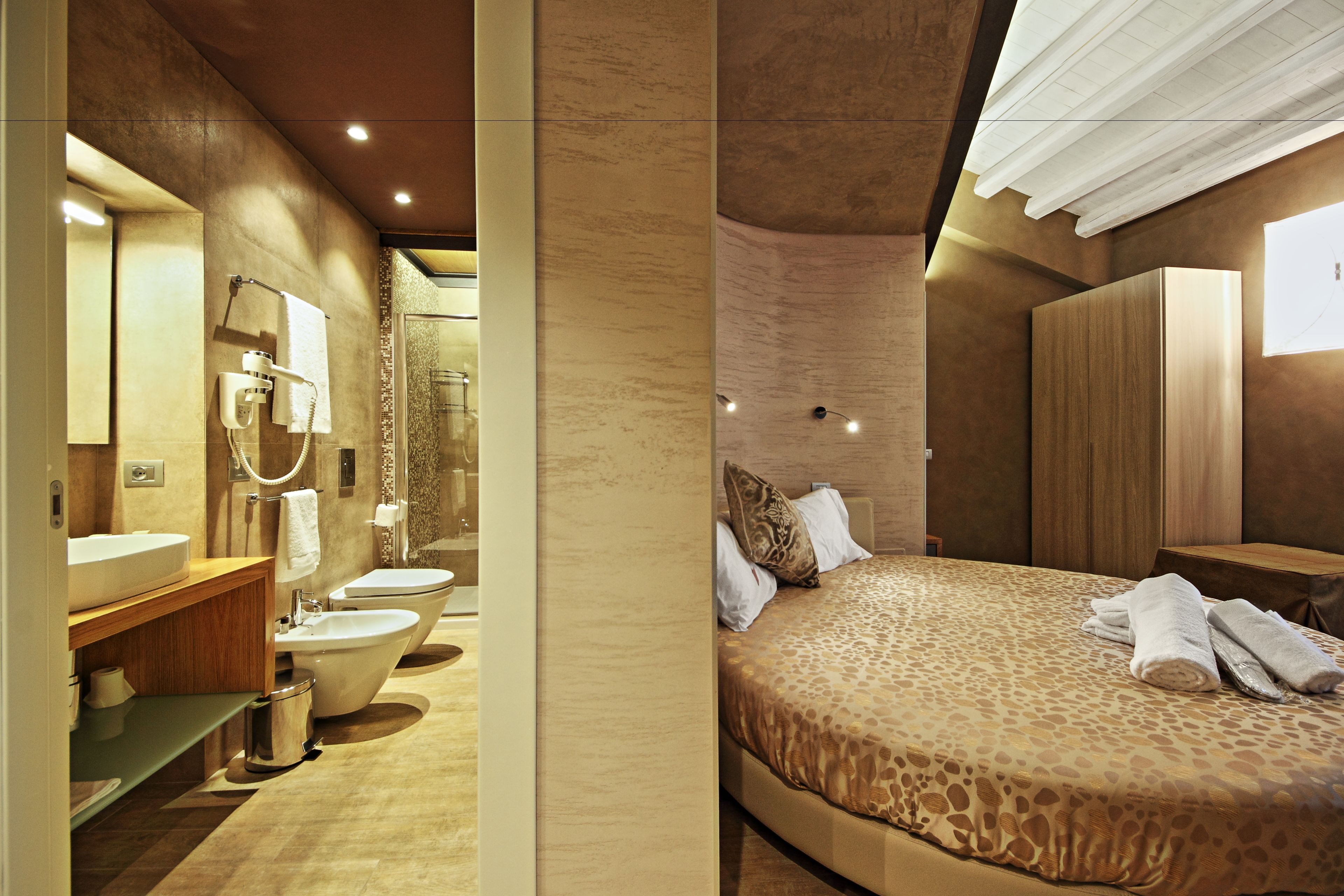 A modern hotel room with a large bed, a bathroom with a bathtub, and a wardrobe.