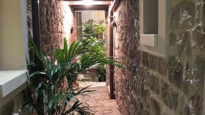 A narrow stone corridor with a tiled floor, leading to a room with a wooden ceiling and a window. - Notti O'Tunn (Geraci Siculo)