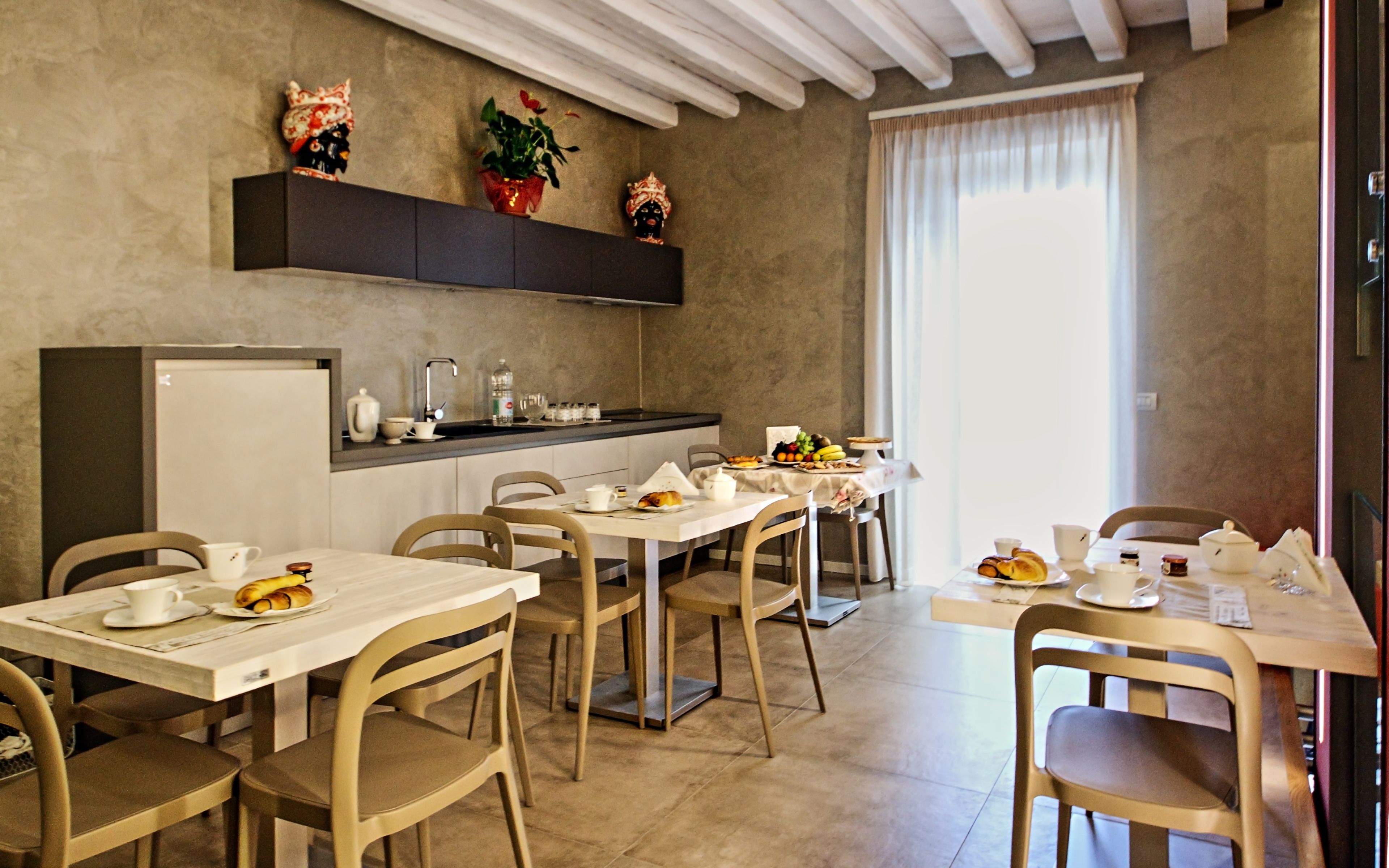A dining area with tables and chairs, a kitchen counter with various items, and a window with curtains.
