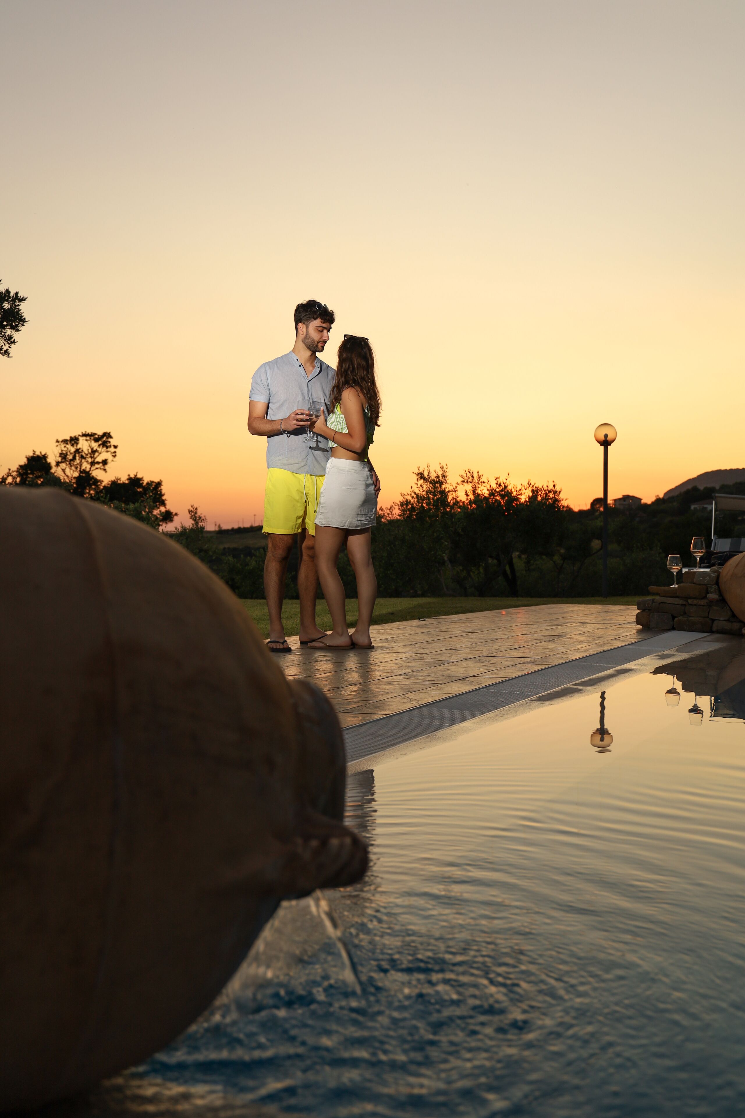 Un couple se tient près d’une piscine au coucher du soleil.
