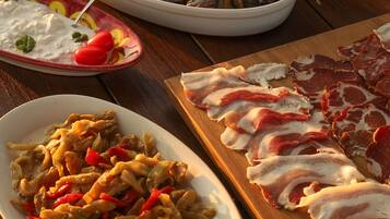 Un tavolo di legno con diversi piatti, tra cui verdure grigliate, carne a fette e una ciotola di pomodorini.