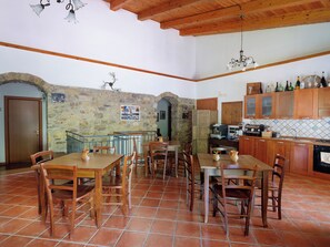 A spacious dining area with wooden tables and chairs, a stone wall, and a kitchen with wooden cabinets and tiled backsplash. - L' Aia Resort (Trentinara)