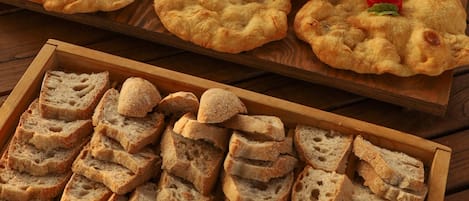 A wooden table with a tray of sliced bread and a wooden board with round, golden-brown flatbreads garnished with cherry tomatoes.