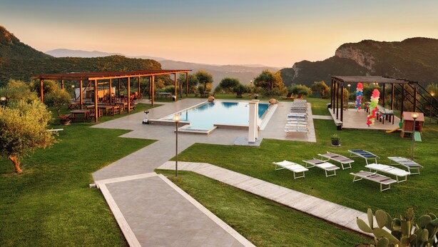 A pool area with lounge chairs, a pergola, and a view of mountains. - L' Aia Resort (Trentinara)