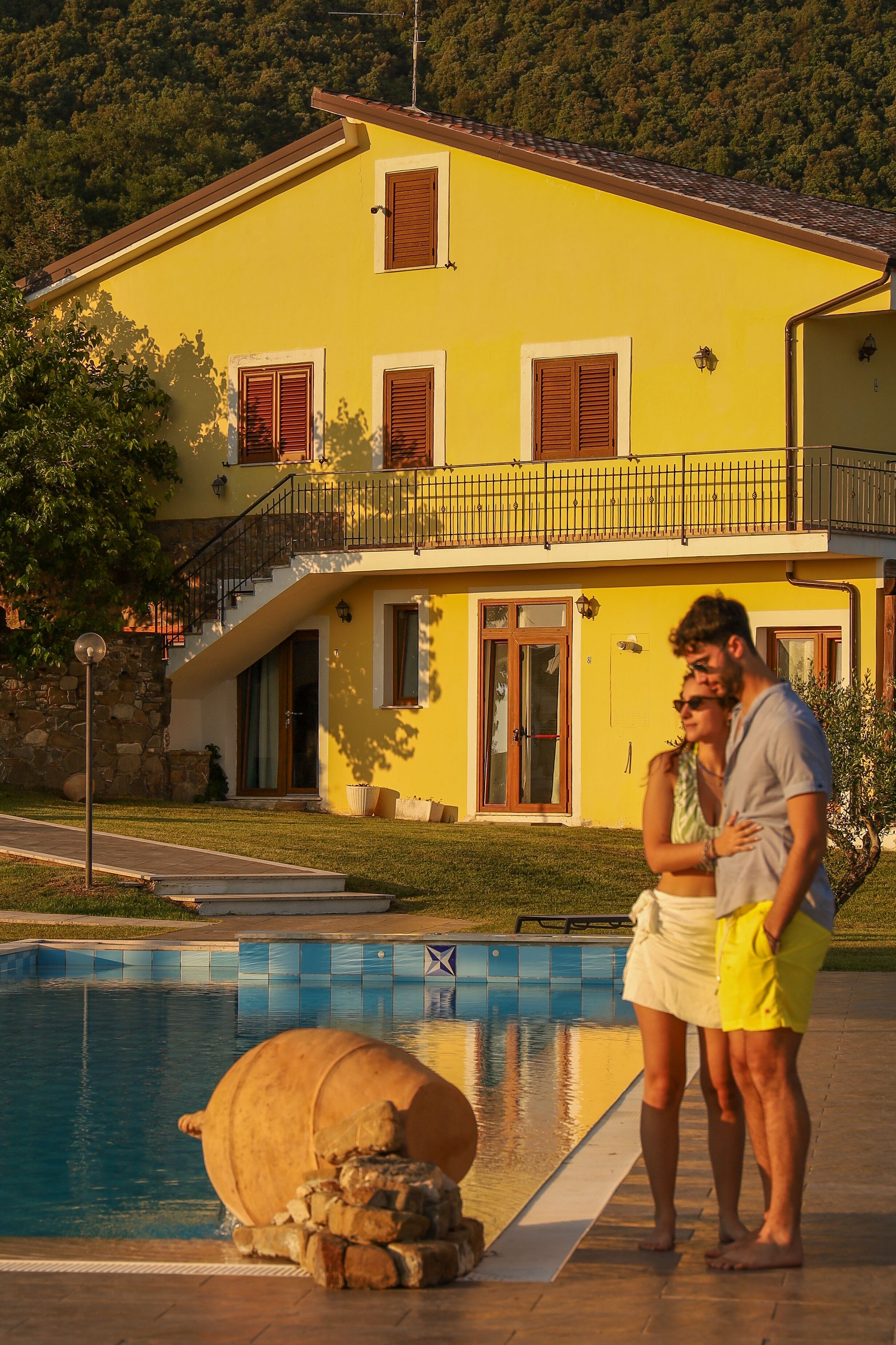 Une maison jaune avec une piscine, un mur en pierre et un balcon.