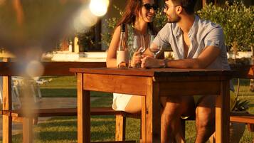 A couple sitting at an outdoor wooden table with a glass of wine, with buildings in the background.