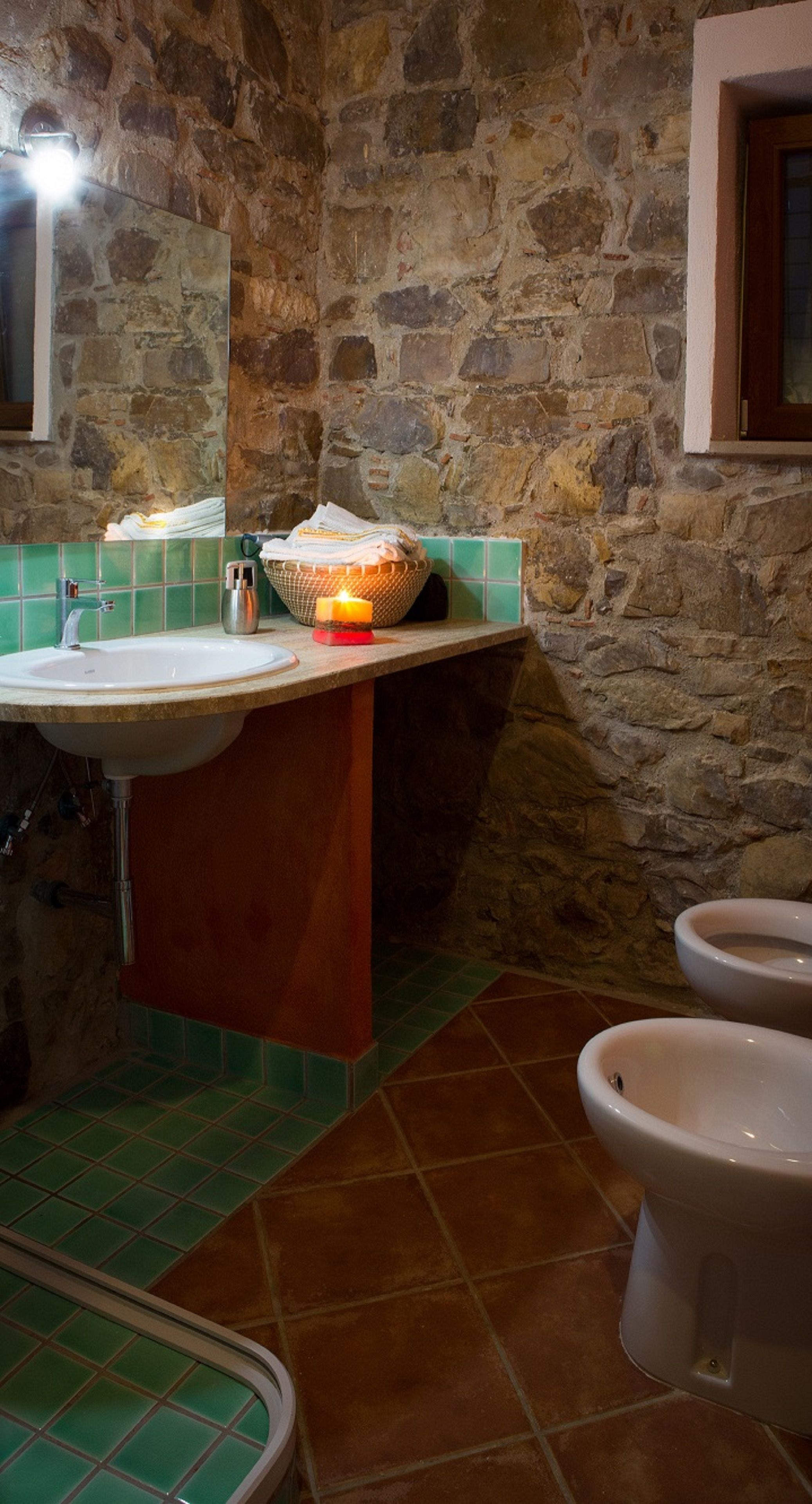Ein Badezimmer mit Steinwand, Waschbecken, Spiegel und zwei Pissoirs.