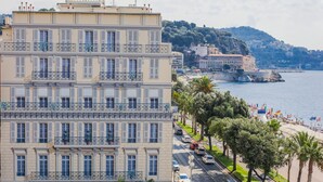 Un edificio de varios pisos con balcones, vista al mar y una playa en el fondo.