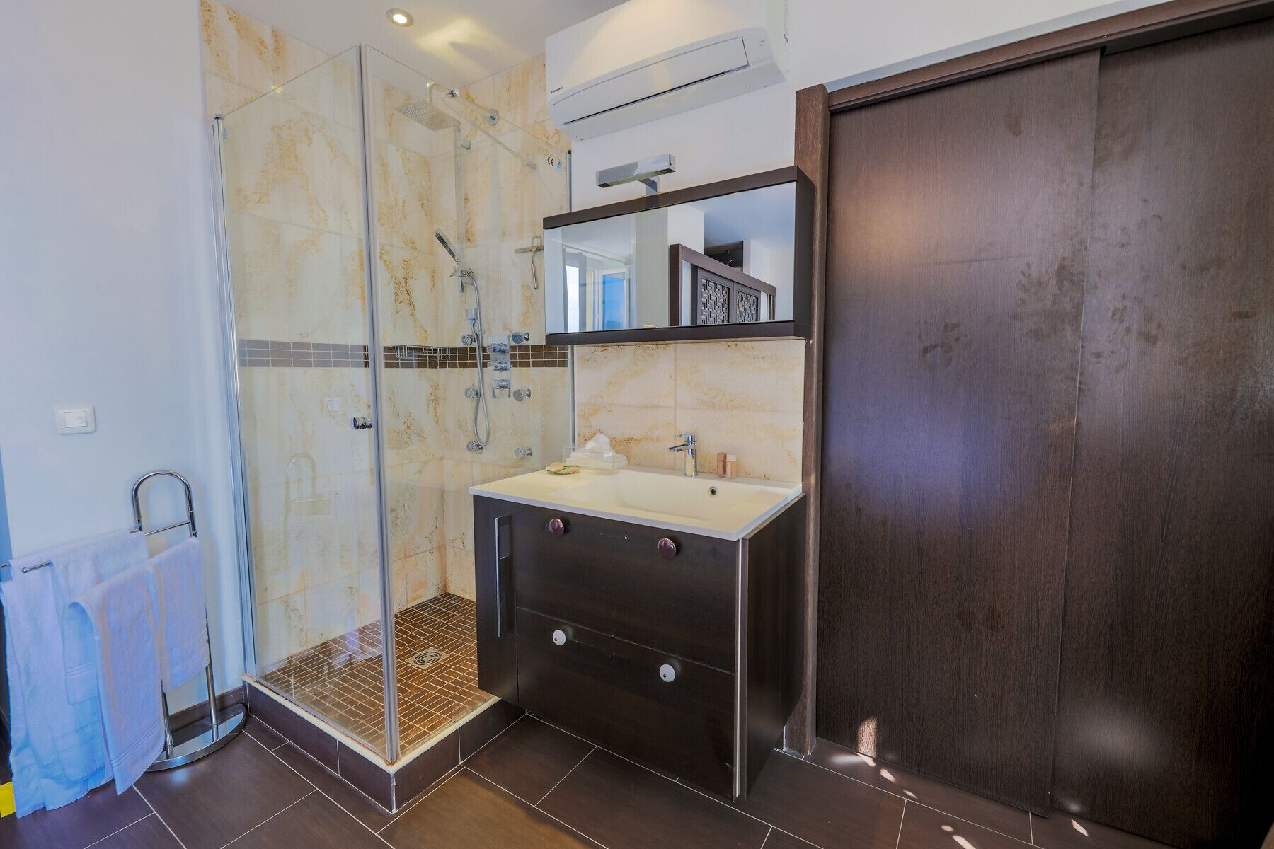 Une salle de bain moderne avec une douche à parois de verre, un meuble-lavabo avec un miroir et une porte en bois foncé.