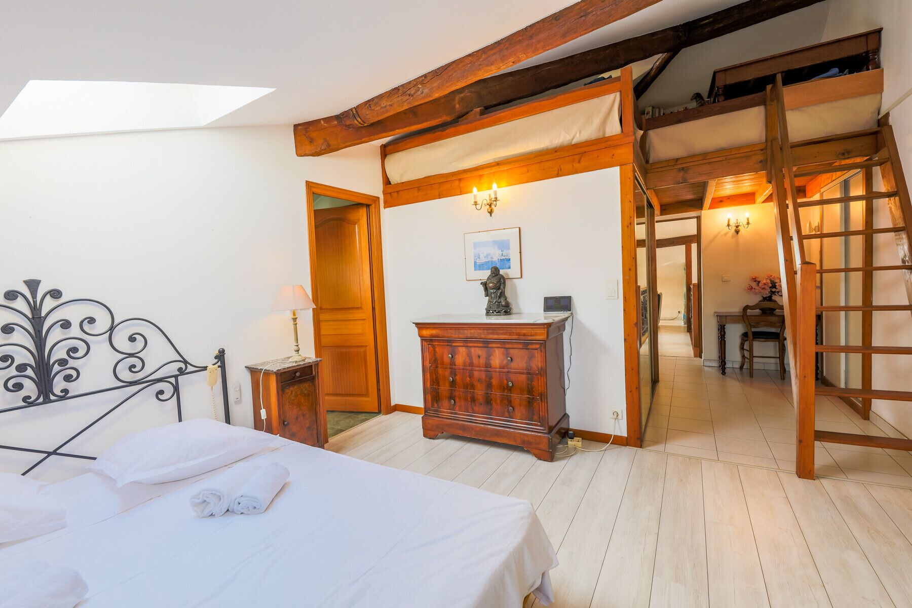 Ein Schlafzimmer mit einem Bett, einem Holzschrank und einem Schreibtisch mit Lampe. Eine Treppe führt in einen anderen Raum.