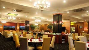 Uma área de refeições de hotel com várias mesas e cadeiras, lustres e um bar.