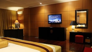Quarto de hotel com cama, escrivaninha, televisão e espelho.