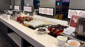 Ein Buffetbereich mit verschiedenen Speisen und Geschirr, darunter Schüsseln, Tassen und Behälter, angeordnet auf einer Theke mit Deckenleuchten.