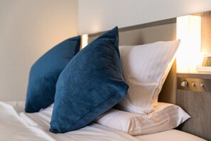 A neatly made bed with two pillows, one blue and one white, and a bedside table with a lamp. - Hotel Mystays Nagoya Nishiki (Nagoya)