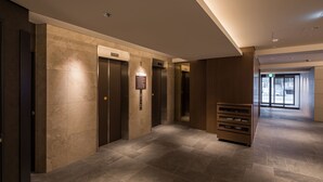 Eine moderne Hotelhalle mit drei Aufz ügen, einer hölzernen Bank und einem gefliesten Boden.